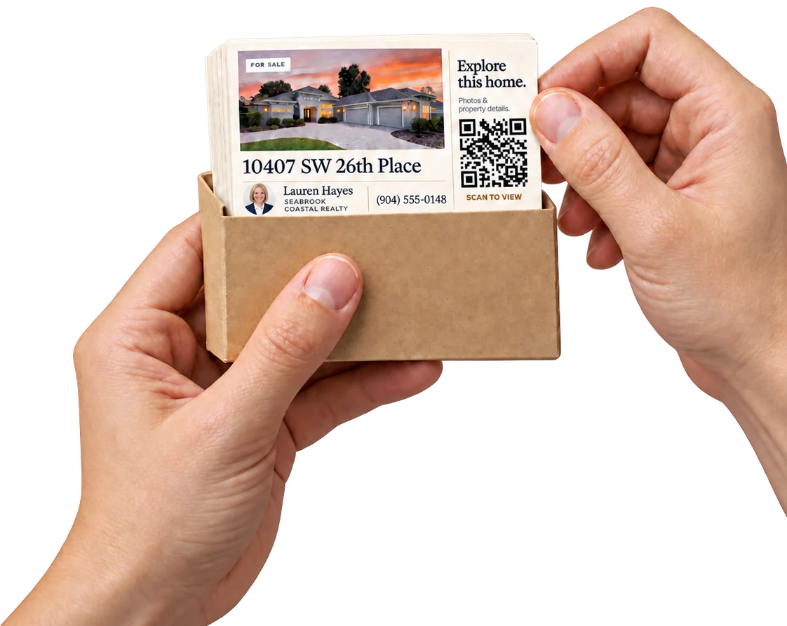 Two hands holding a kraft box of printed QR listing cards for 10407 SW 26th Place, pulling one card out.